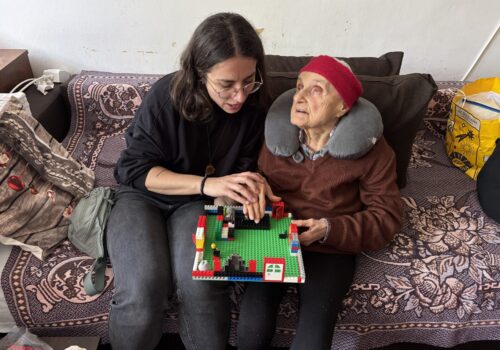 Ana Costache, trainer de mobilitate și orientare, îi arată unei bătrâne o hartă Lego. Stau pe canapea.