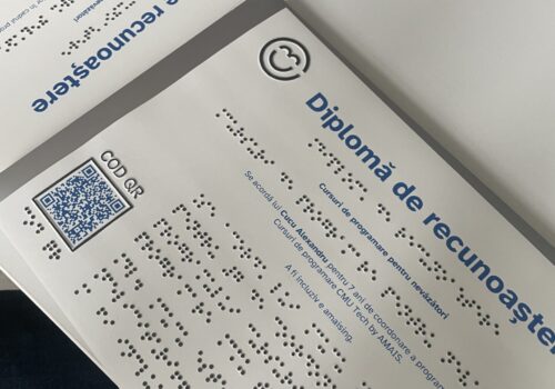Fotografie cu două diplome scrise în alb-negru și în Braille ale mentorilor din cadrul cursului. Au aniversat 7 ani de mentorat și CMU Tech