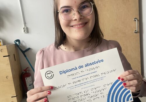 Portret cu Carmen, absolventă, poartă ochelari și o bluză roz și zâmbește. Ține în mâini diploma sa