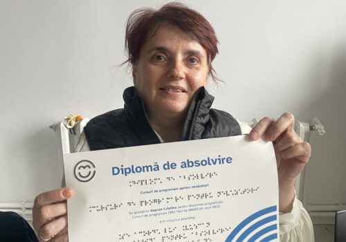 Portret cu Cristina, absolventă, are părul roșcat prins în coadă la spate și ține în mâini diploma. Zâmbește
