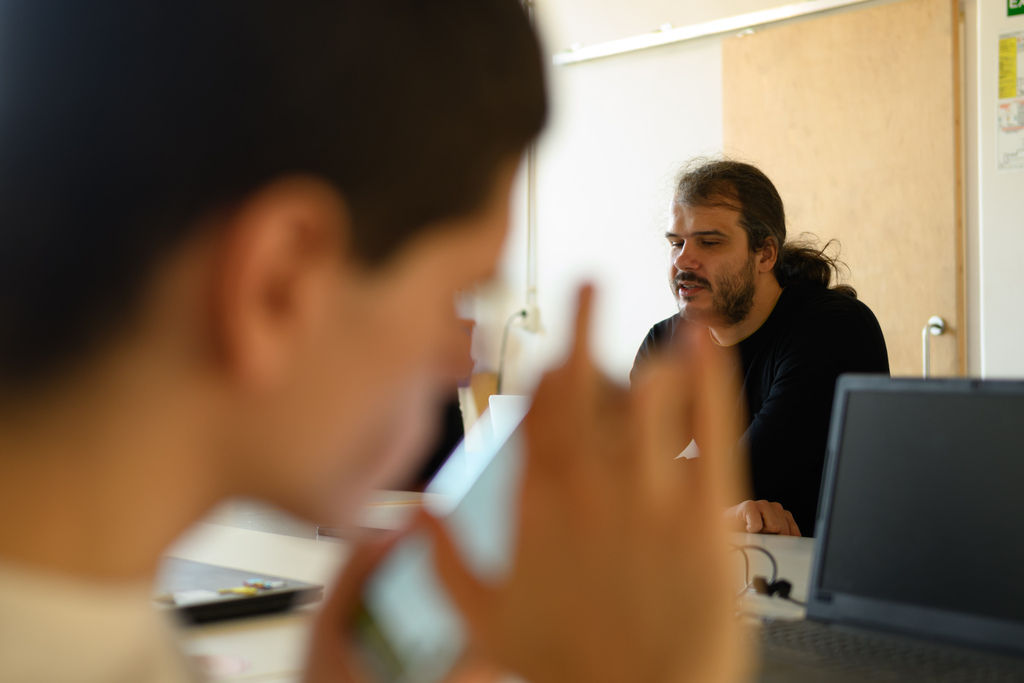 în prim plan, alex matei tastează pe un telefon. în fundal, alex cucu tastează la un laptop.